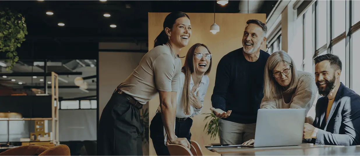 Five Diverse Colleagues Smiling Around A Laptop In A Modern Office